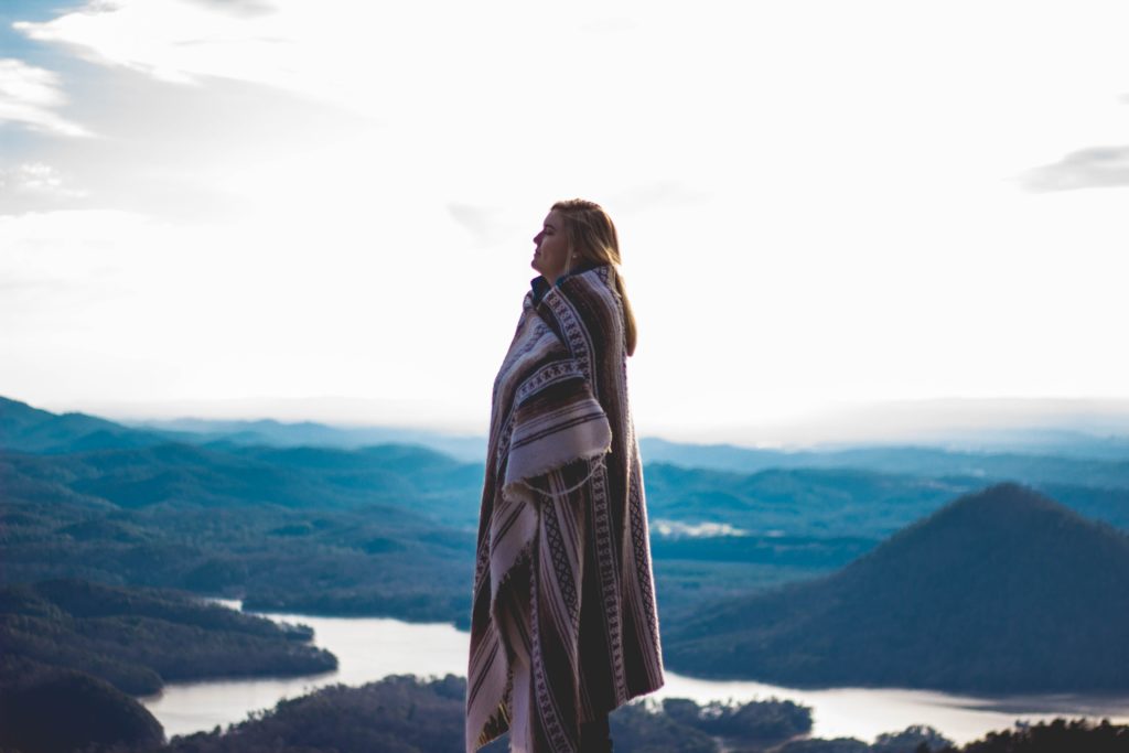 jeune femme entourée d'un plaid regardant le paysage montagneux